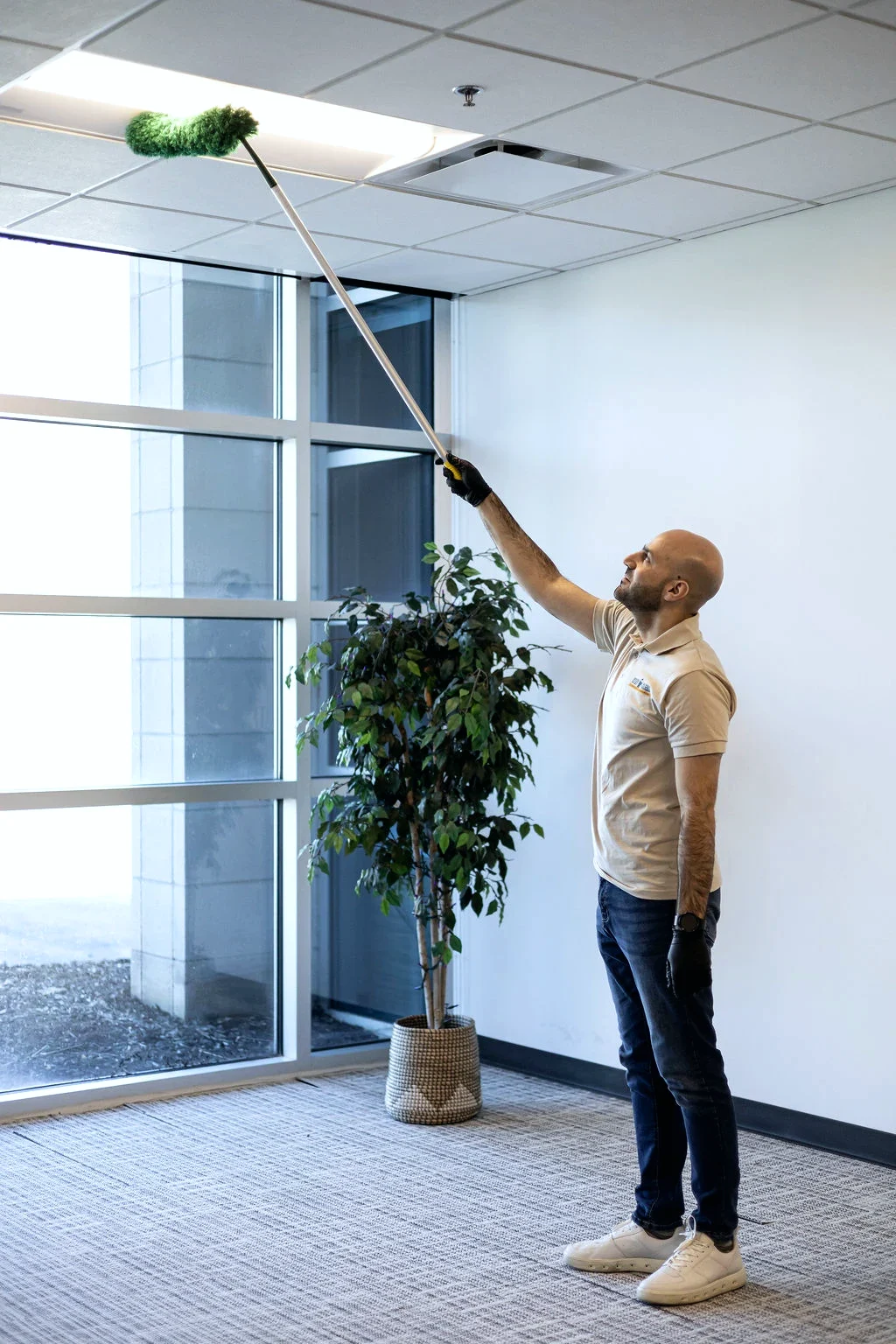 Technician high-dusting an office ceiling vent with an extension duster