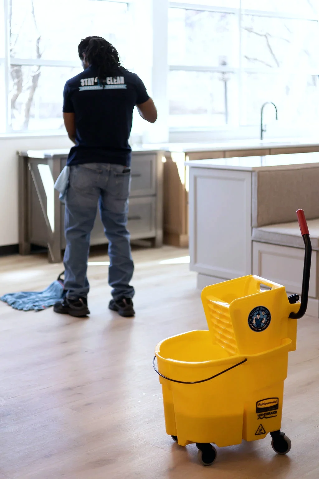 A cleaner working alone in an empty commercial break area with an unattended mop bucket