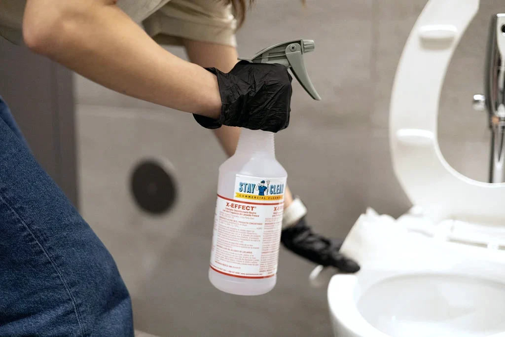 Gloved technician applying disinfectant in a commercial restroom